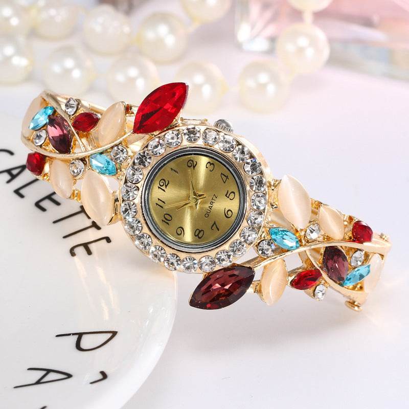 Gold-tone ladies bracelet watch with red and blue stones and crystal bezel round dial