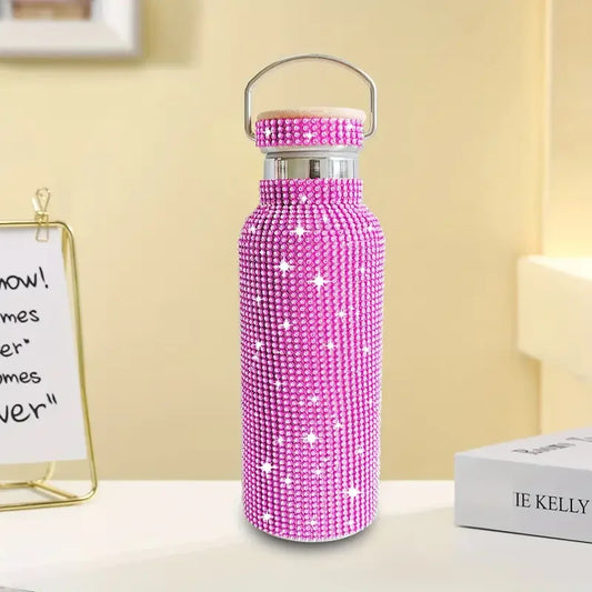 Pink rhinestone water bottle with lid, sparkling bling accessory on a desk indoors.