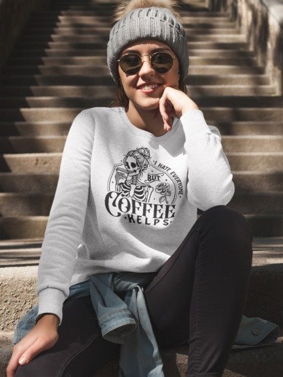 Model sitting on steps wearing a white I Hate Everyone But Coffee Helps skeleton graphic sweatshirt