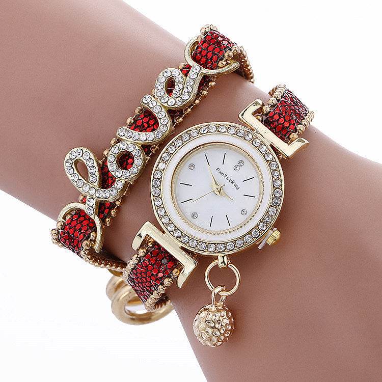 Rhinestone bracelet watch with round white dial, gold-tone bezel, and red gem bracelet links