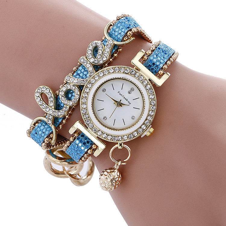Rhinestone bracelet watch with round white dial, gold-tone bezel, and blue gem strap links