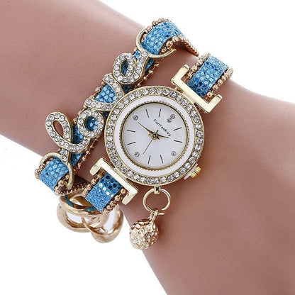 Rhinestone bracelet watch with round white dial, gold-tone bezel, and blue gem strap links