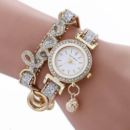 Rhinestone bracelet watch with round white dial, gold-tone bezel, and heart-shaped charms