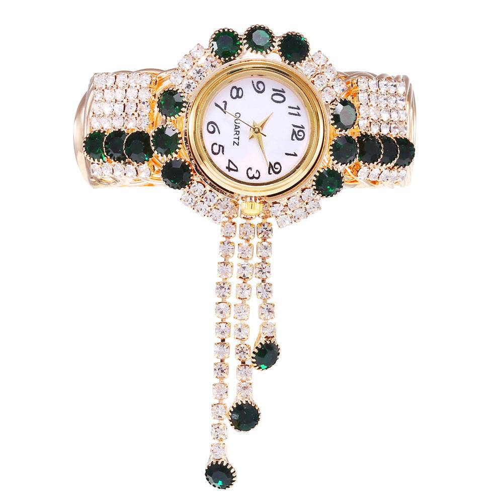 Gold-tone rhinestone bracelet watch with green stones and clear crystals; dangling tassel