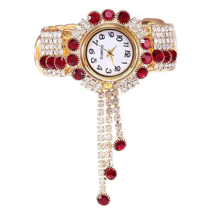 Gold-tone rhinestone bracelet watch with red stones and clear crystal details; dangling links