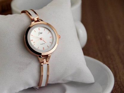 Rose gold watch bracelet close-up with round white dial, red markers, and metal link band