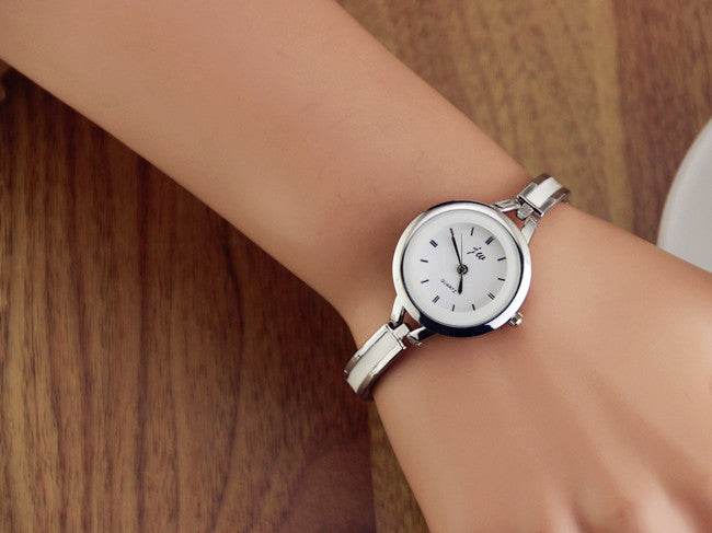 Silver watch bracelet on wrist with round white dial and metal link strap