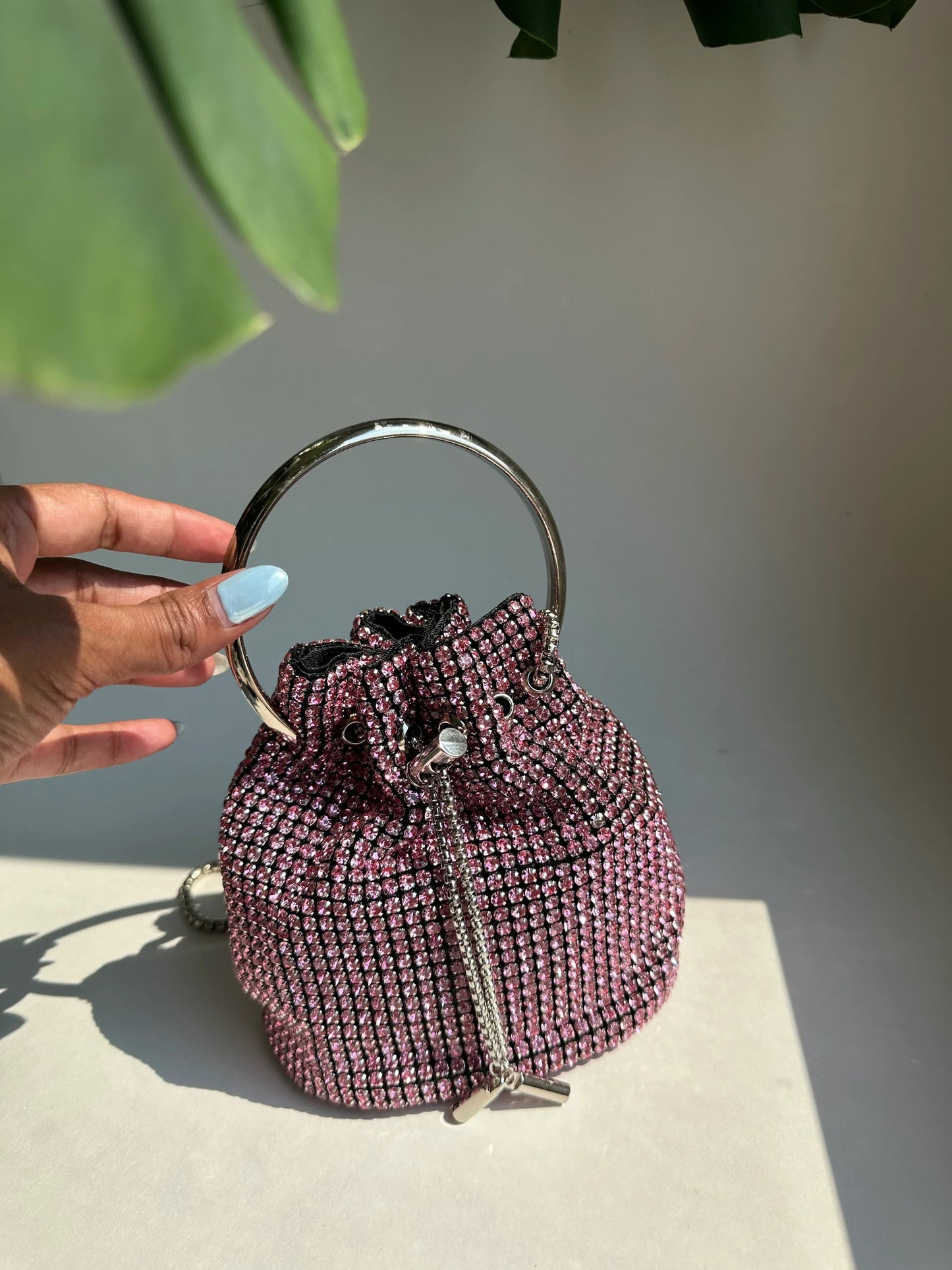 Pink rhinestone bucket bag held by top handle; drawstring closure