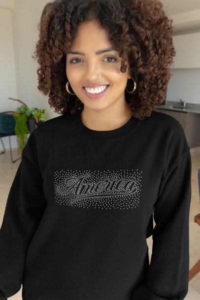 Woman wearing a black sweatshirt with 'America' text in rhinestones, standing in a kitchen.
