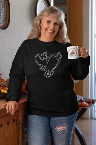 Woman wearing a black sweatshirt with a heart design, holding a mug in a kitchen.