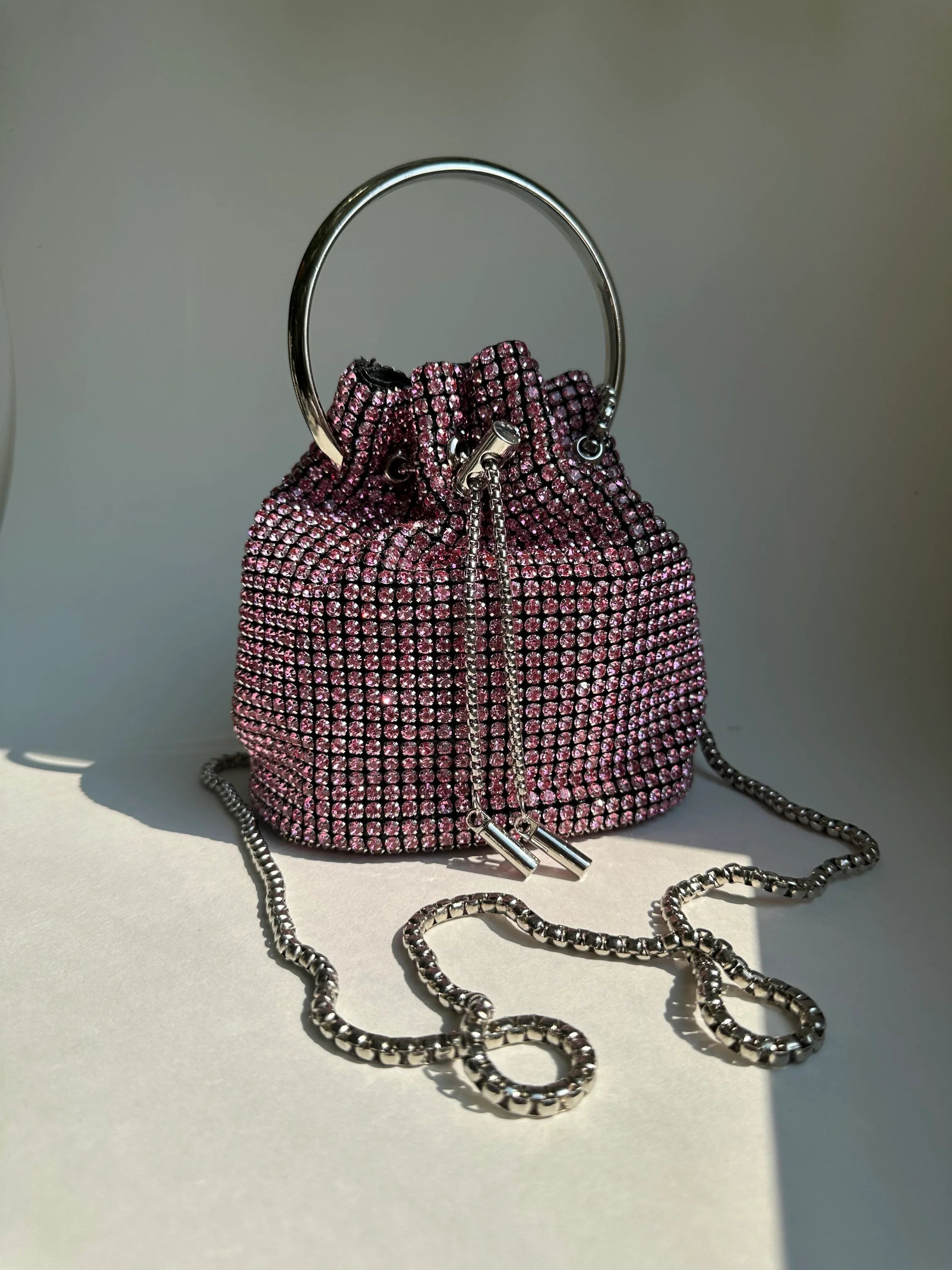 Pink rhinestone bucket bag with chain strap, drawstring closure, and top handle