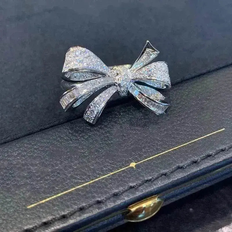 Silver-tone diamond bow ring on dark surface, sparkly ribbon bow design