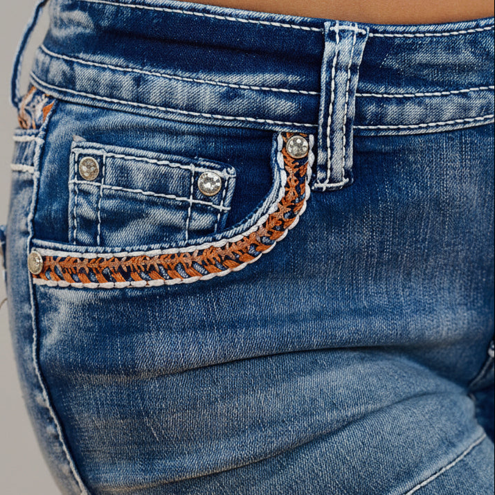 Front pocket with embroidered and rhinestone-studded curved trim on blue denim shorts