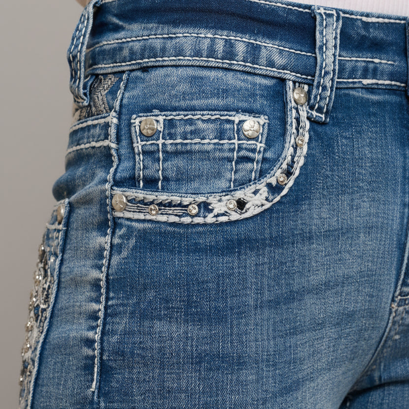 Close-up of blue jeans with decorative stitching and embellishments on a gray background
