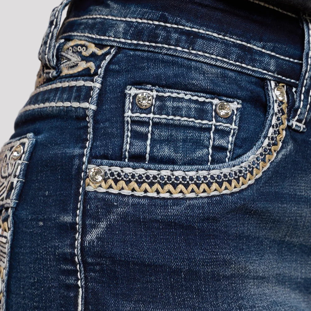 Dark wash denim shorts close-up: jeweled pocket flap with embroidered trim