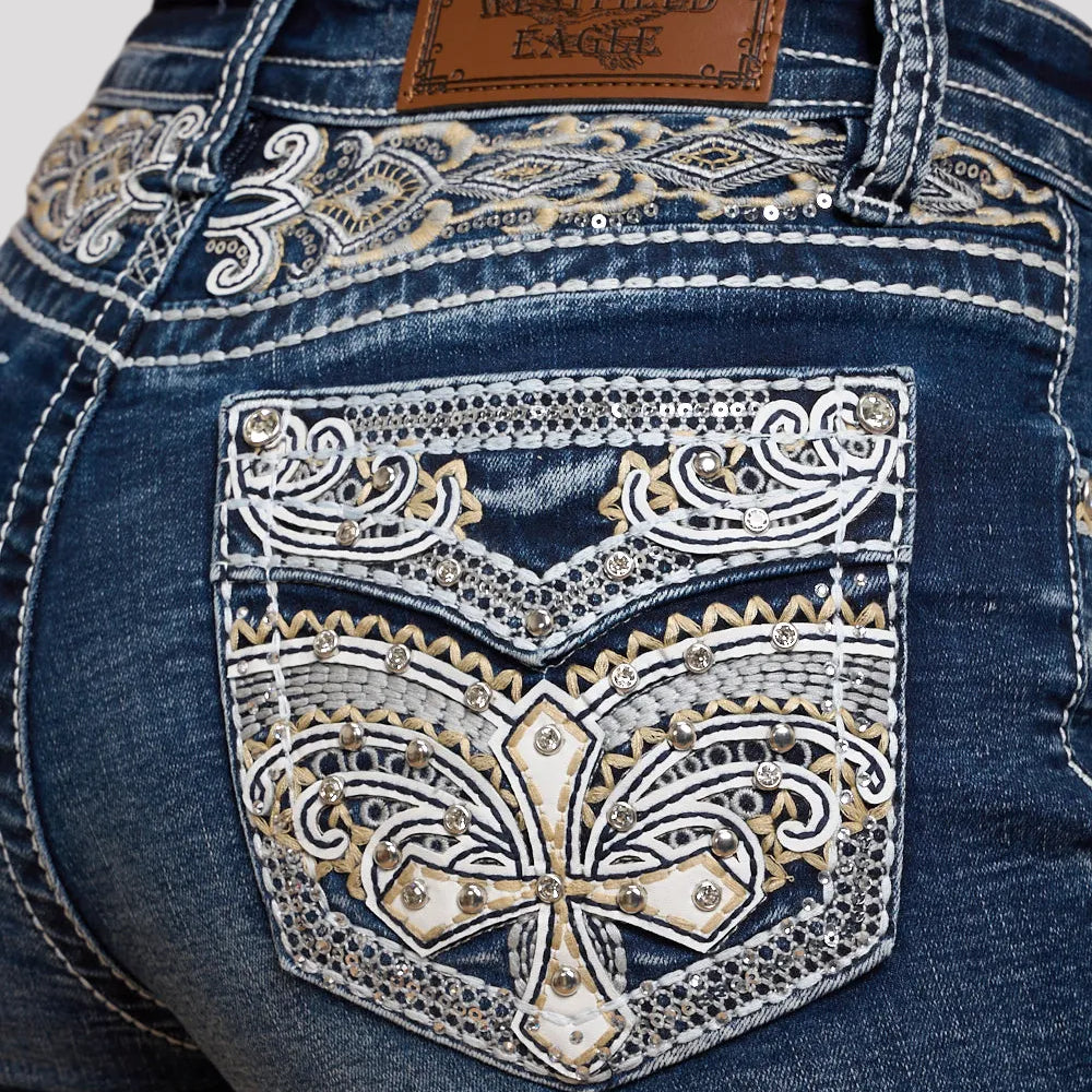 Dark wash denim shorts close-up: ornate embroidered front pocket with rhinestone accents