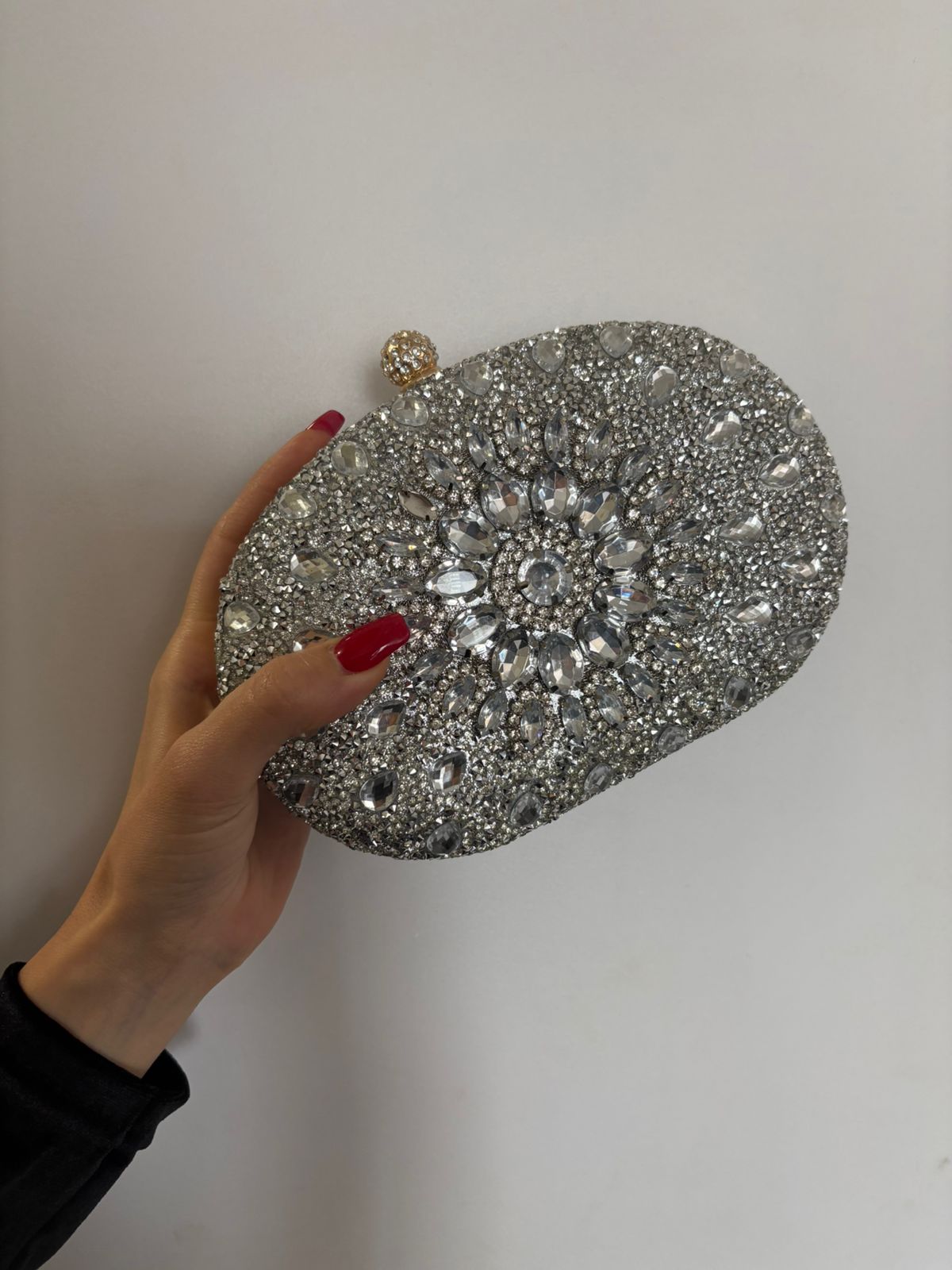 Silver rhinestone oval clutch held in hand, top clasp with gem flower