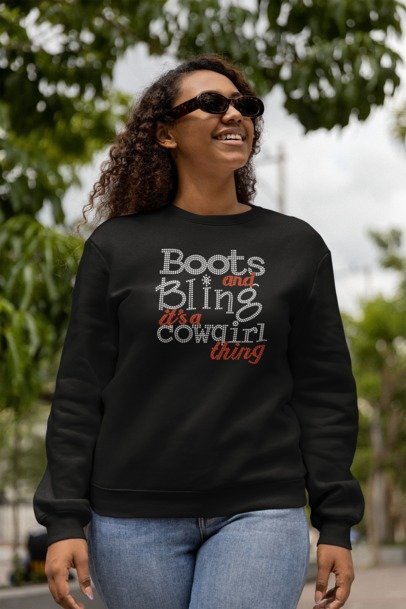Person wearing a black Boots and Bling sweatshirt outdoors with greenery in the background