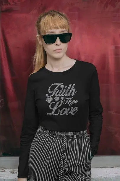 Person wearing a black sweatshirt with 'Faith Hope Love' text and sunglasses against a red curtain background