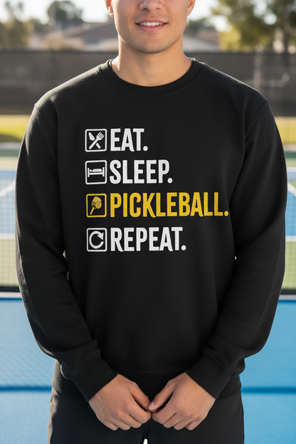 A man wearing a black crewneck sweatshirt with a graphic print on a blue outdoor pickleball court. The graphic reads 'EAT.