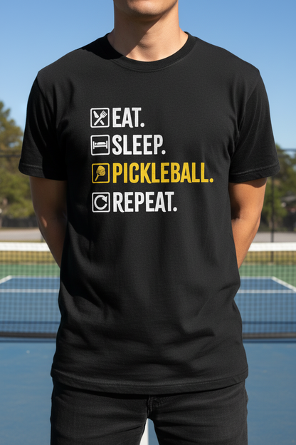 A person wearing a black short-sleeve T-shirt with a printed slogan on a pickleball court. The shirt reads 'EAT.