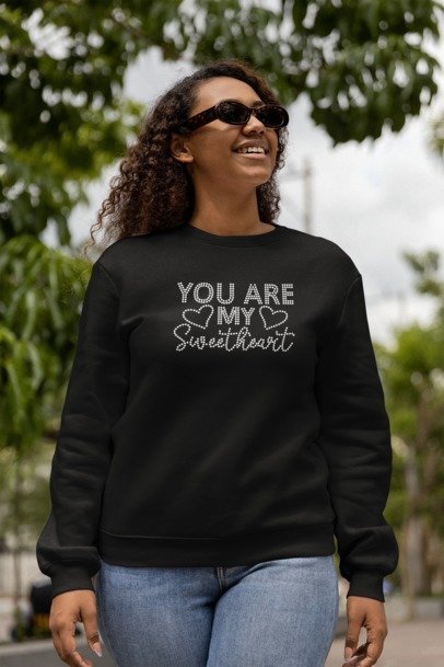 Woman wearing a black sweatshirt with 'You are my sweetheart' text outdoors.